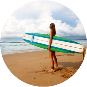 Chica en una playa con una tabla de surf para explicar la depilación láser con la exposición solar